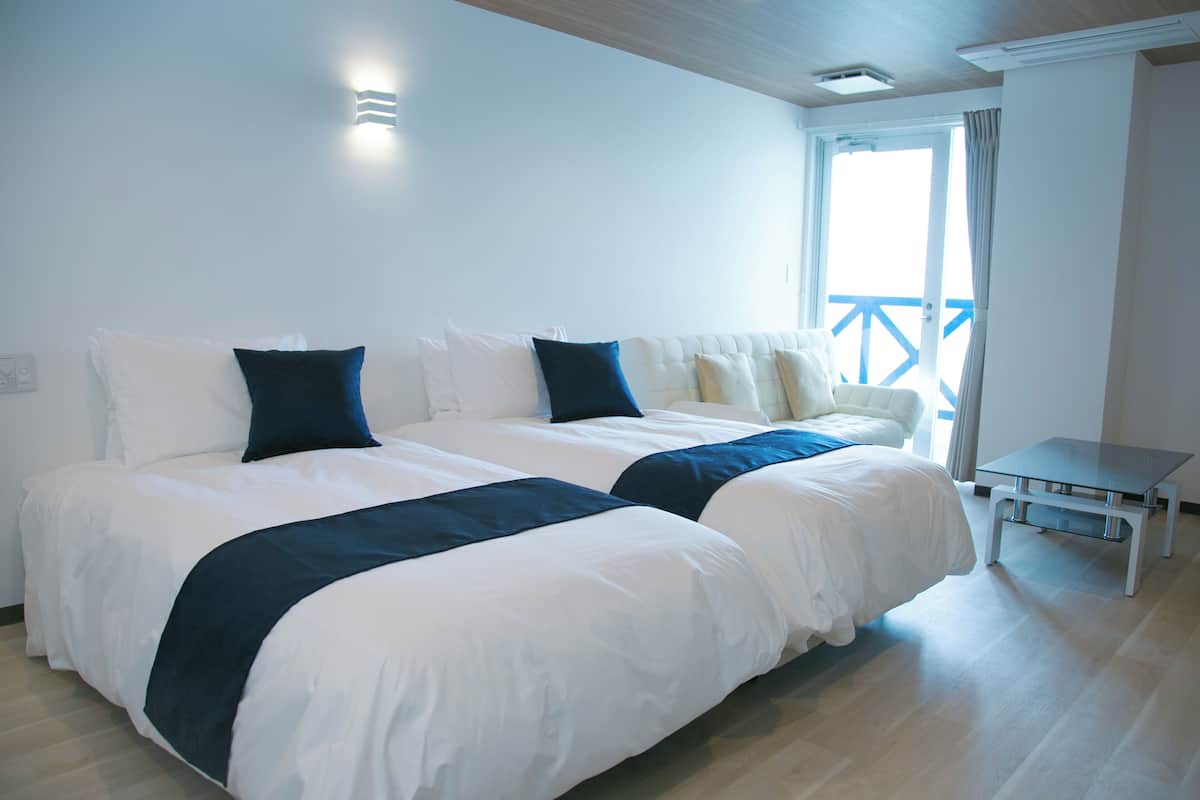 Une chambre d’hôtel avec deux lits, une petite table et un balcon doté d’une rambarde bleue.
