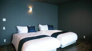 A double bed with white and dark blue bedding, a wall-mounted light, and a dark wooden floor.