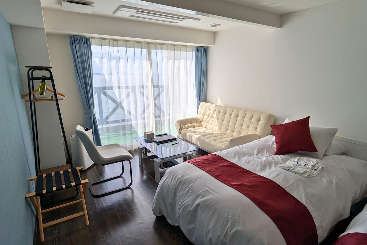 Une chambre d’hôtel avec un lit, une chaise, une petite table et une fenêtre avec des rideaux.
