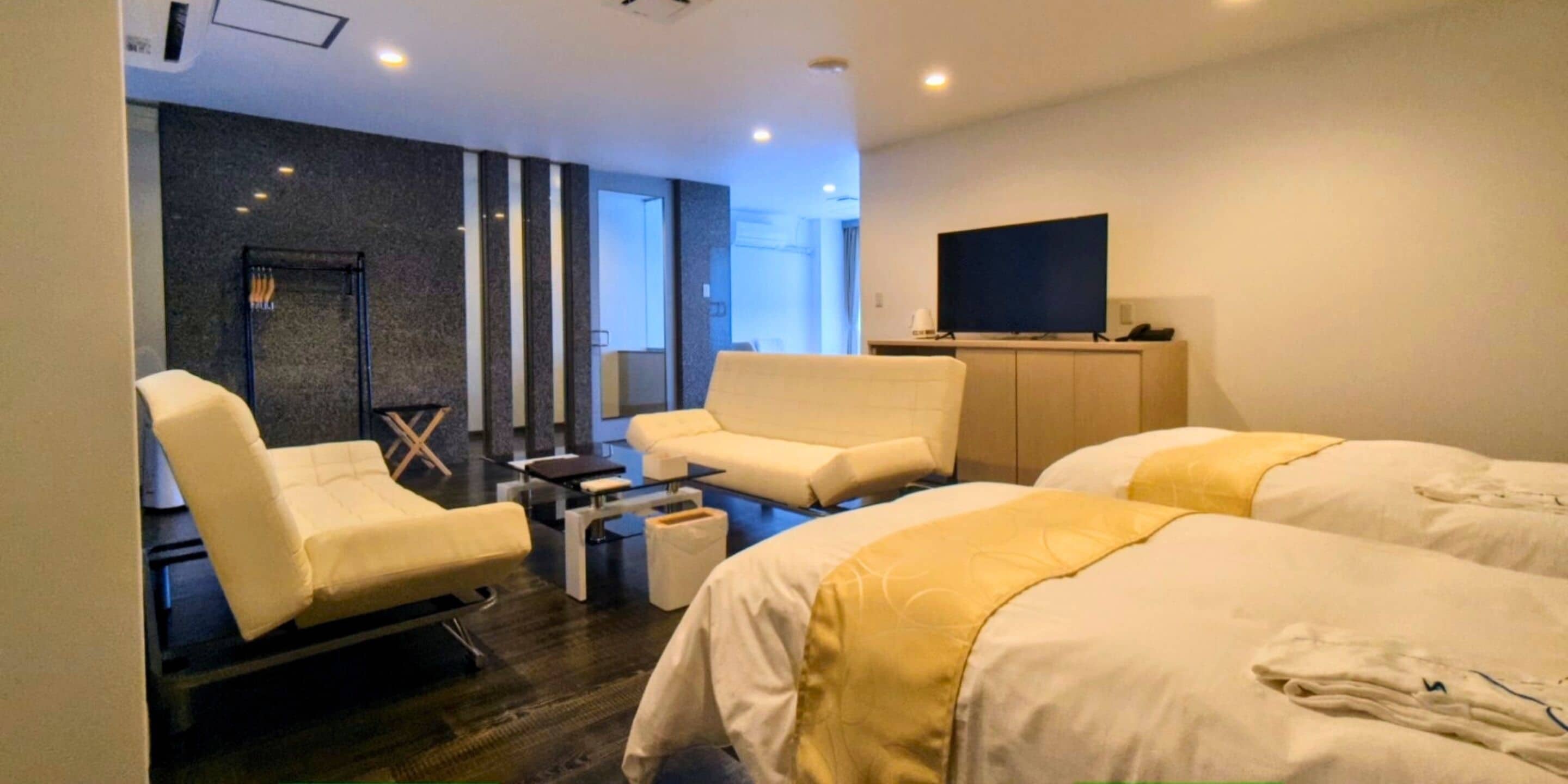 A modern hotel room with a sofa, two beds, a TV, and a small table.