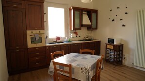 A kitchen with wooden cabinets, a table with chairs, a stove, and a microwave. - Cleo Viola (Ancona)