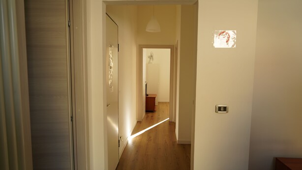 A hallway with wooden flooring, a door on the left, and a light fixture on the right. - Cleo Viola (Ancona)