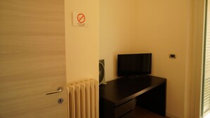 A room with a wooden door, a black desk with a television, and a radiator. - Cleo Viola (Ancona)