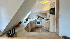 A compact kitchen with a sloped ceiling, a built-in oven, a microwave, and wooden cabinets. - 100 m² in Bester Fernblicklage im Haus Schneekappe (Winterberg)