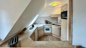 Eine kleine Küche mit schräg versiegelter Decke, einem Einbauofen, einer Mikrowelle und Holzschränken.