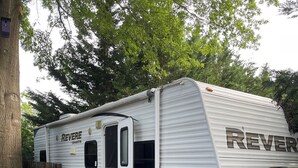 A REVERSE RV parked on a wooden deck with a chair and a white lattice screen nearby. - Nature's Haven Tiny Home (Bear)