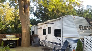 A recreational vehicle (RV) with a grill and a deck area. - Nature's Haven Tiny Home (Bear)