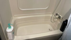 A small, white bathtub with a handheld showerhead, a bottle of shampoo, and a black bottle on the side. - Nature's Haven Tiny Home (Bear)