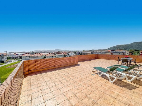 A rooftop terrace with tiled flooring, a brick wall, and outdoor seating. - Apartamento Solamaza Ático (Arnuero)