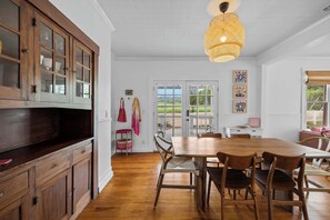 Un comedor con mesa y sillas de madera, un aparador grande con puertas de vidrio y una lámpara colgante.