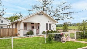 Ein bungalow mit Veranda, einem eingezäunten Garten und einem rosafarbenen Fahrrad.