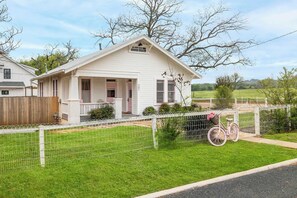 Una casa de un piso con porche, patio cercado y una bicicleta rosa.