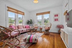Una habitación con un sofá rosa, sillas de mimbre, una mesa redonda y un mueble para la televisión.
