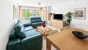 A modern living room with a sectional sofa, a TV, and a dining area with a table and chairs. - Apartamento Solamaza con Terraza XL (Arnuero)