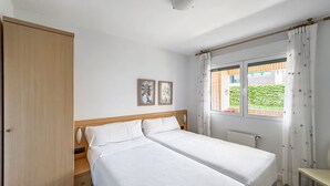 A bedroom with two beds, a wooden wardrobe, a window with curtains, and two framed pictures on the wall. - Apartamento Solamaza con Terraza XL (Arnuero)