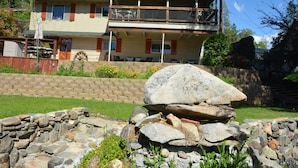 Una casa de dos pisos con un balcón, un muro de piedra y un patio con césped.