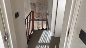 A narrow stairway with wooden beams, a stone wall, and a white door.