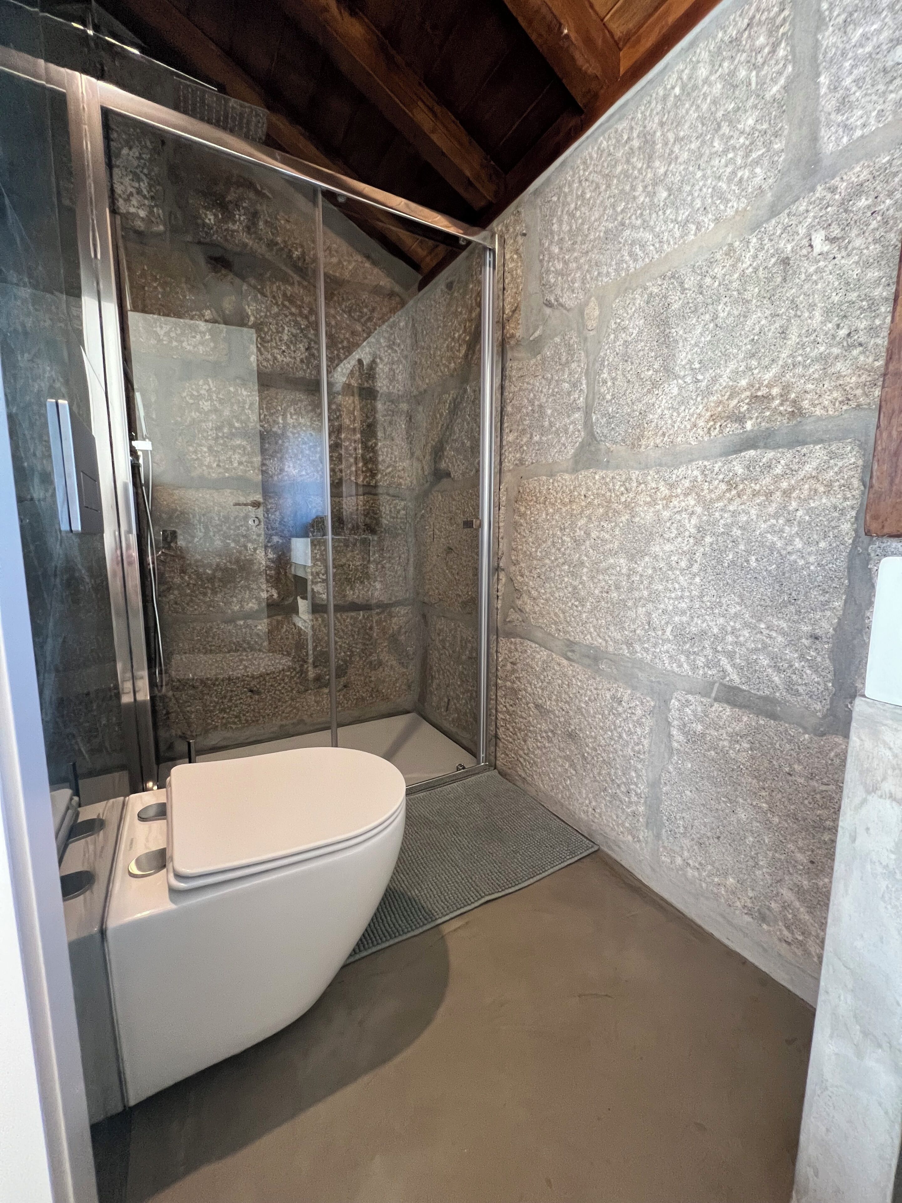 A modern bathroom with a glass-enclosed shower, a white toilet, and a stone wall.