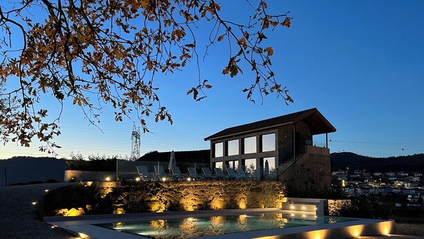 A modern building with a pool, lounge chairs, and a stone wall.