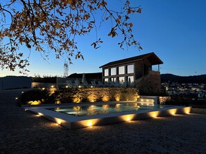 A modern building with a pool, lounge chairs, and a stone wall. - Casa da Eira (Povoa de Lanhoso)