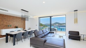 A modern living room with a sectional sofa, dining area, and large windows offering a view of a coastal landscape. - Hedera Estate, Hedera A25 (Dubrovnik)