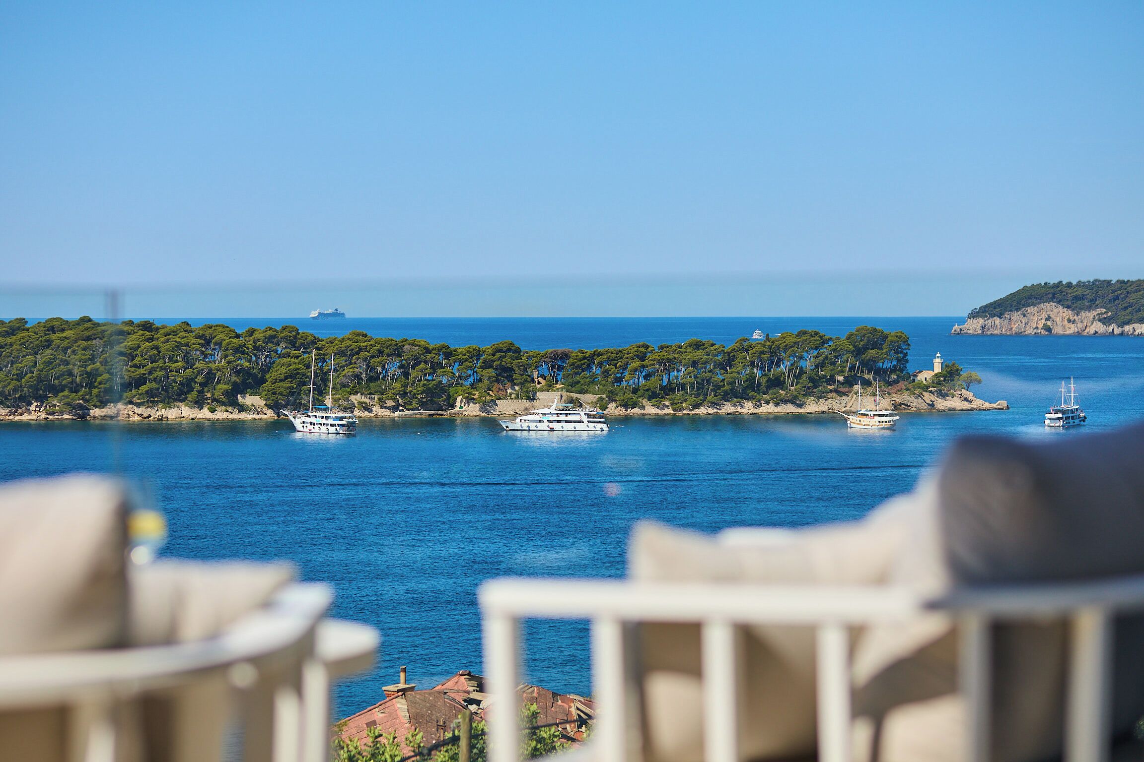 Une vue sur la côte, avec une rangée de bateaux sur l’eau, un phare et une île boisée.