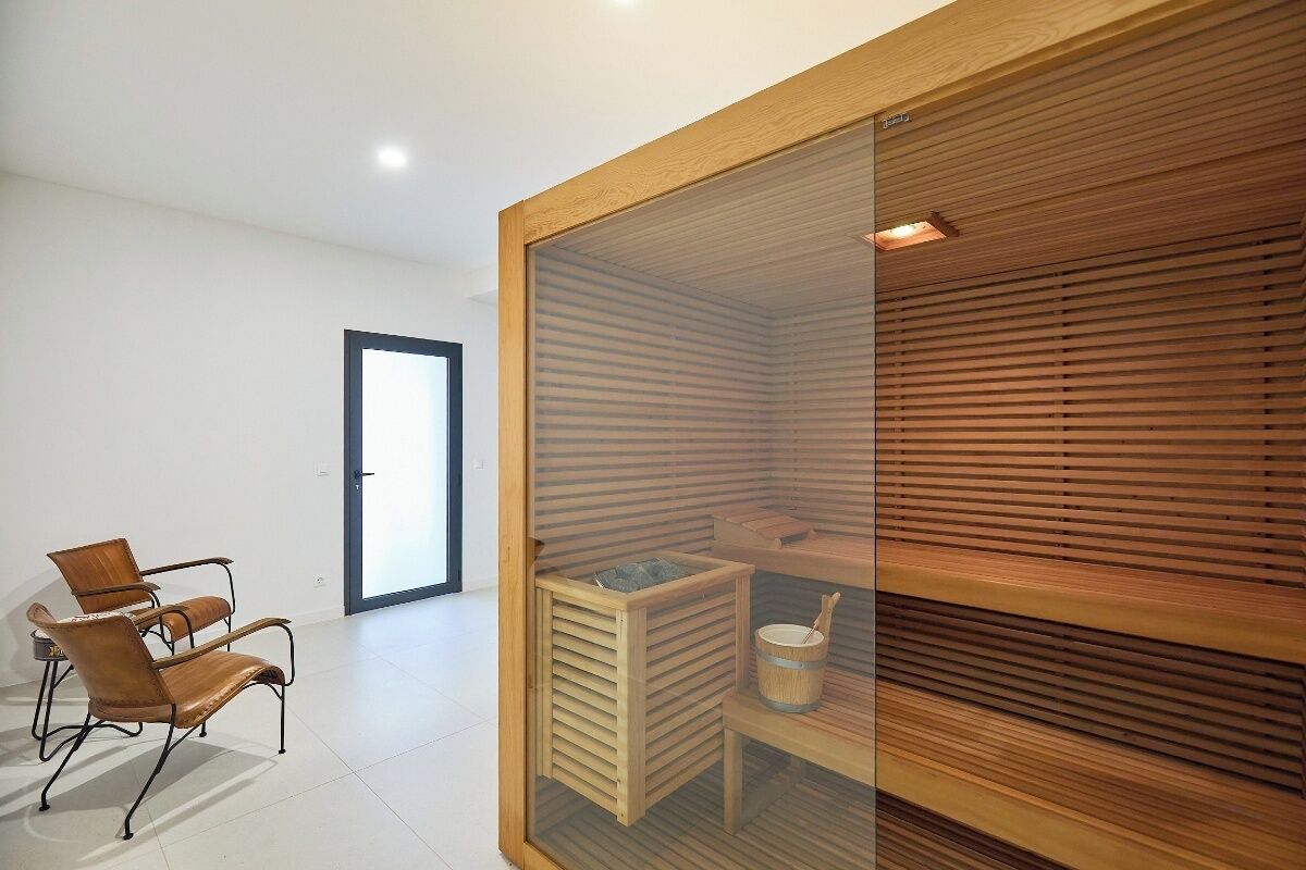 A modern room with a glass partition, wooden slatted wall, a wooden cabinet, and two leather chairs.