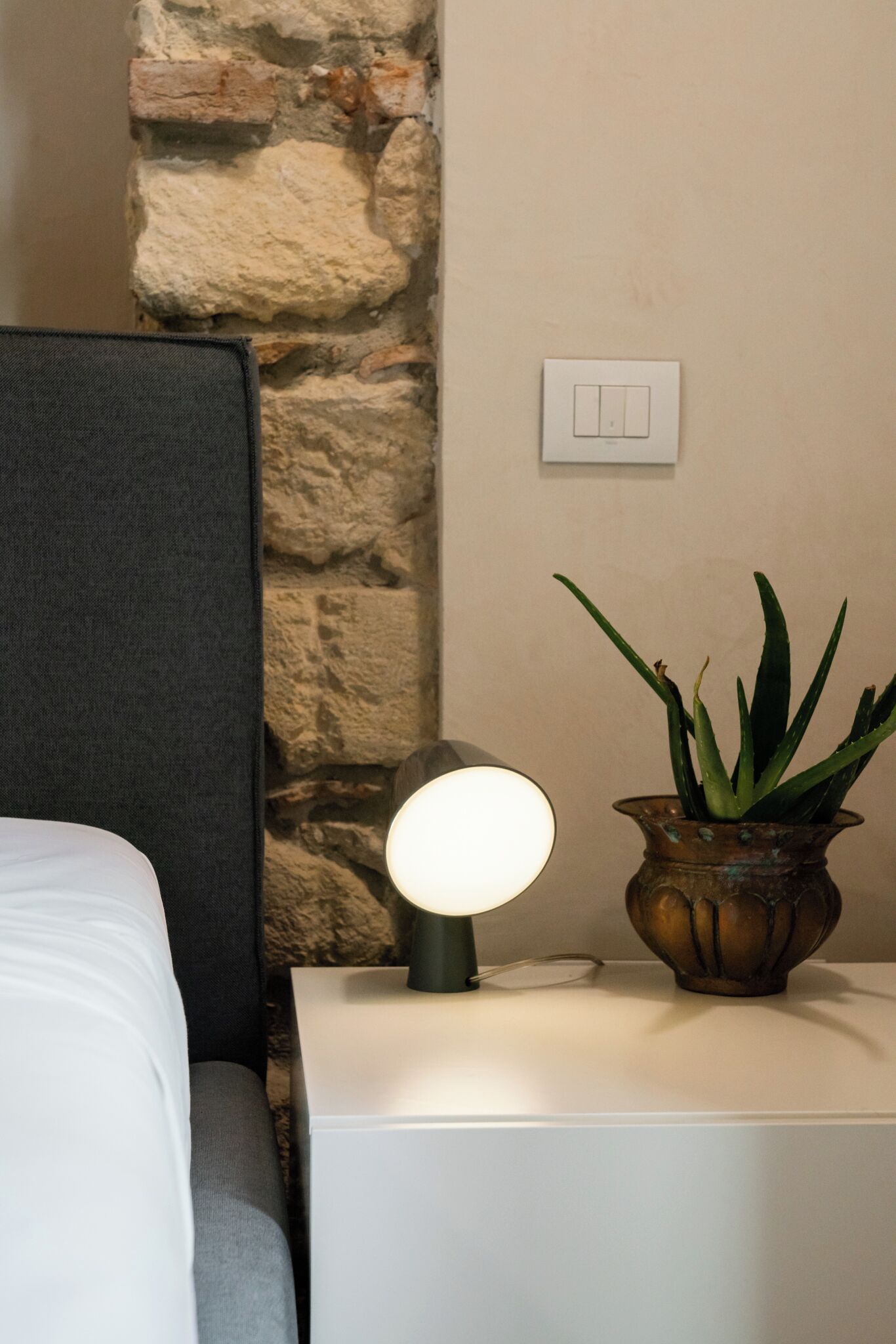 Un dormitorio ordenado con cama, lámpara de noche y planta en maceta.