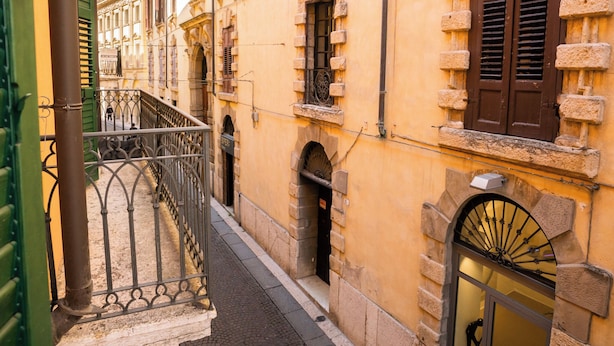 Une rue étroite, bordée d’une rambarde en métal, et un immeuble à la façade en pierre, avec une fenêtre ornée d’une grille métallique.