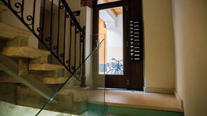 Un escalier avec des marches en pierre et une rampe en verre, menant à une porte en bois surmontée d’un portail en métal.
