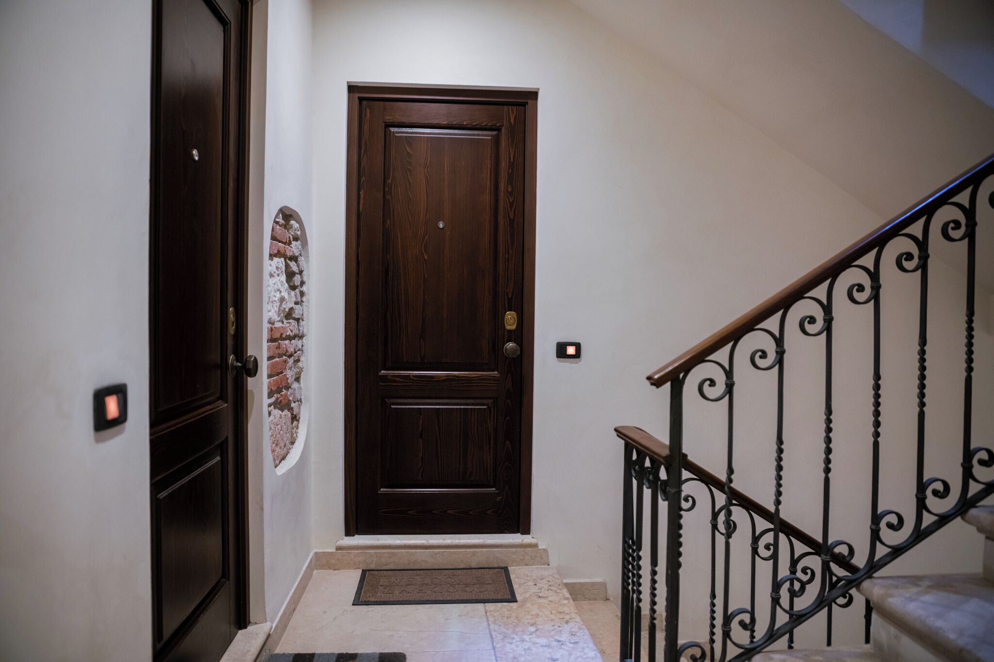 A wooden door with a doorknob, a small mat at the base, and a wall-mounted light switch.