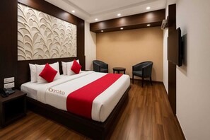 A hotel room with a large bed, two bedside tables, a TV, and a small seating area with two chairs and a table. - Hotel Himshri By Ovata (Dehradun)