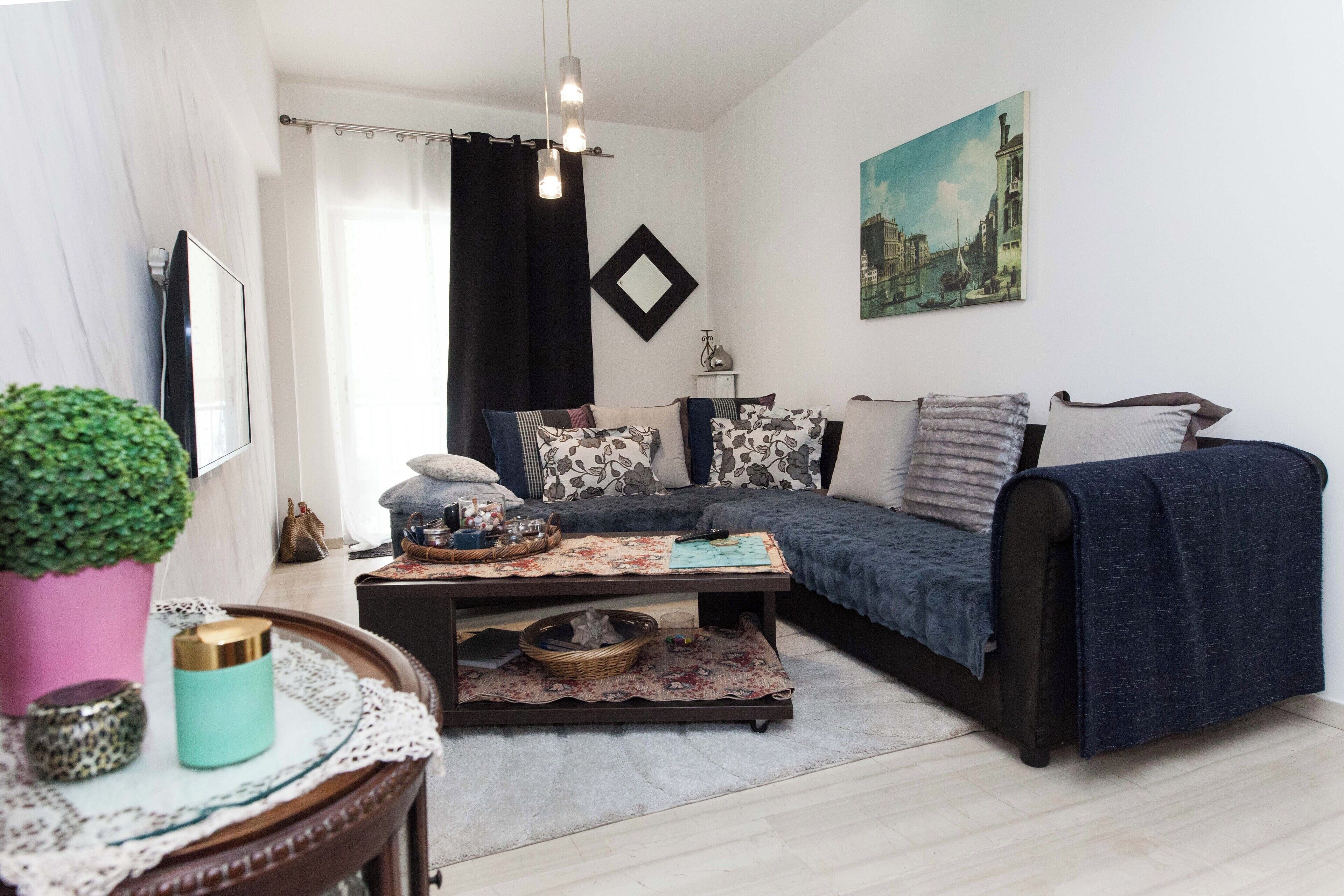 A cozy living room with a dark blue sofa, a coffee table with decorative items, a potted plant, and a painting on the wall.