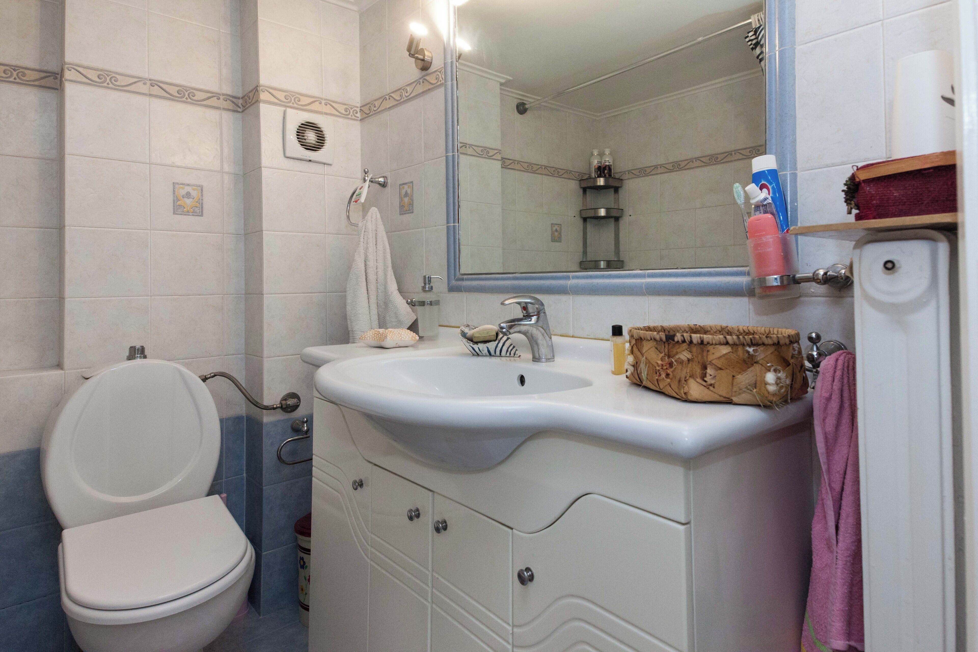 A bathroom with a toilet, sink, mirror, and towel rack.
