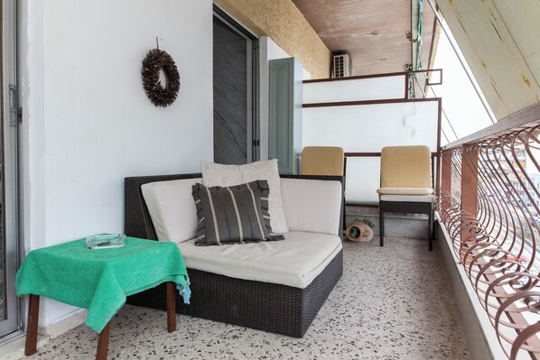 Un balcon avec un canapé en osier, une petite table recouverte d’une nappe verte et une rambarde en métal.