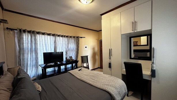 Una habitación de hotel con una cama, televisión, escritorio y armario.