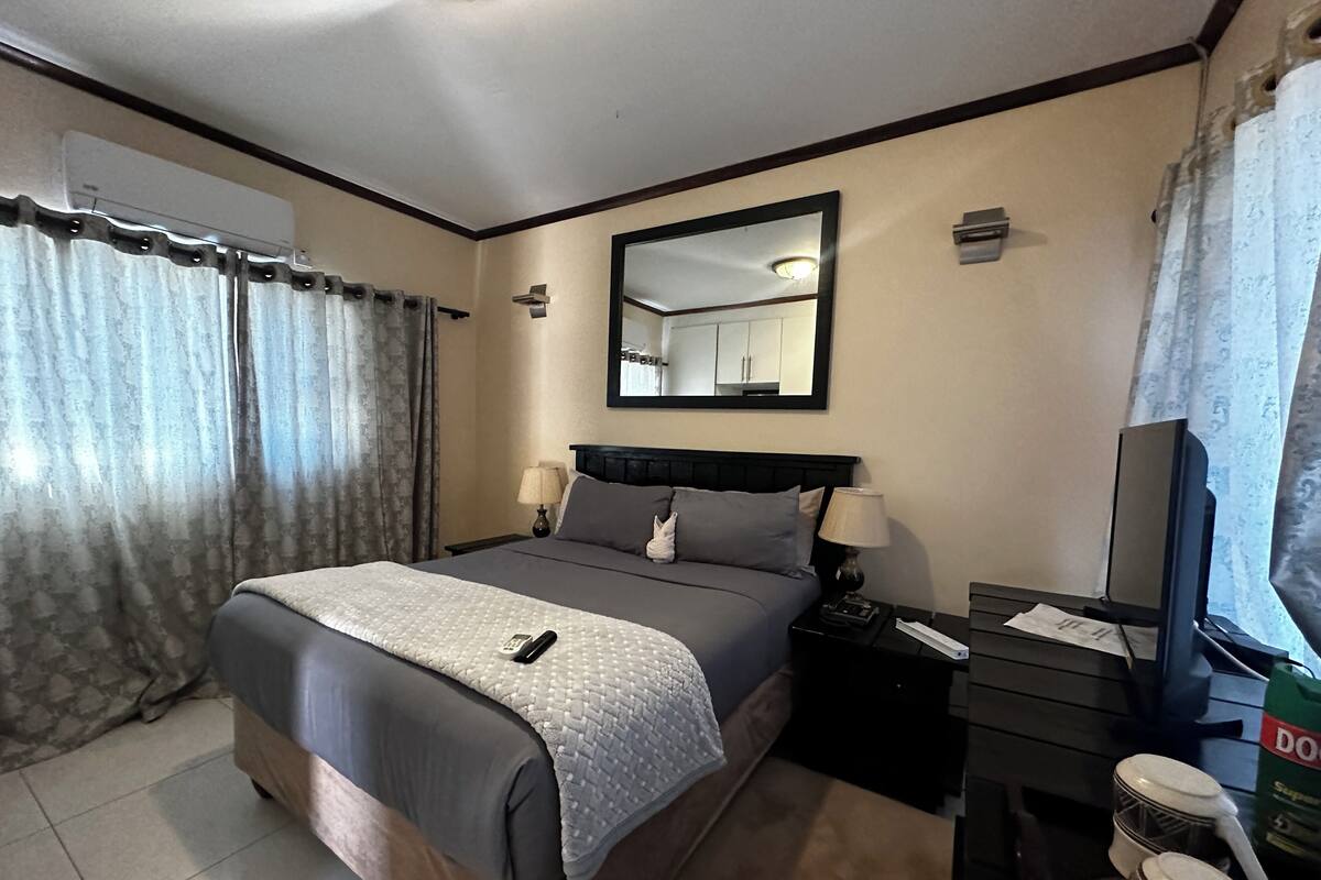 Habitación de hotel con cama, lámparas de noche, escritorio con computadora, espejo y ventana con cortinas.