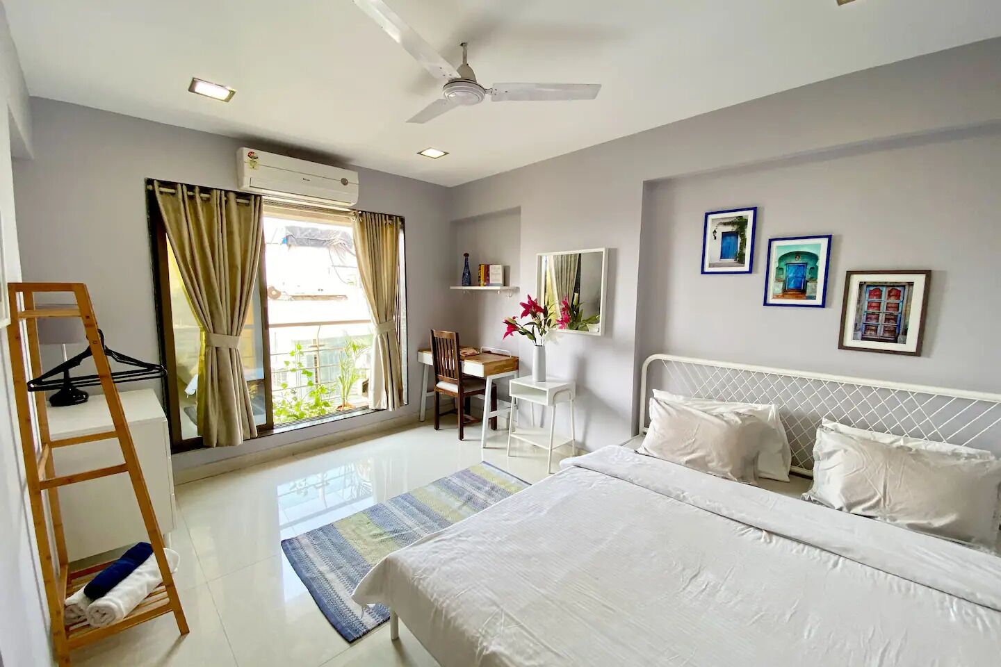 Una habitación de hotel con cama, escritorio, silla, escalera, ventana con cortinas, aire acondicionado y ventilador de techo.