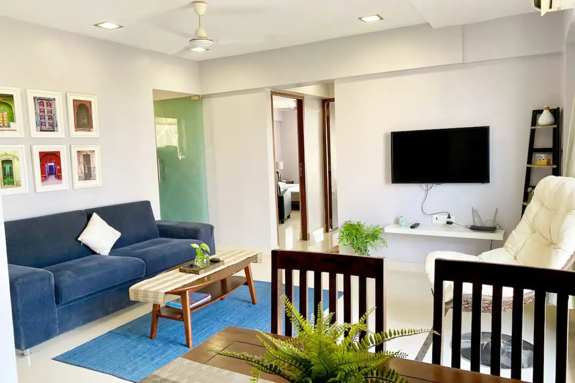 Una sala de estar moderna con un sofá azul, una mesa de centro de madera, un sillón blanco y un televisor montado en la pared.