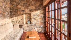 A cozy room with a stone wall, a wooden bench, a sofa, and a large window with a view of a cityscape. - Elounda Monastiri Cretan sea View House With Pool (Agios Nikolaos)