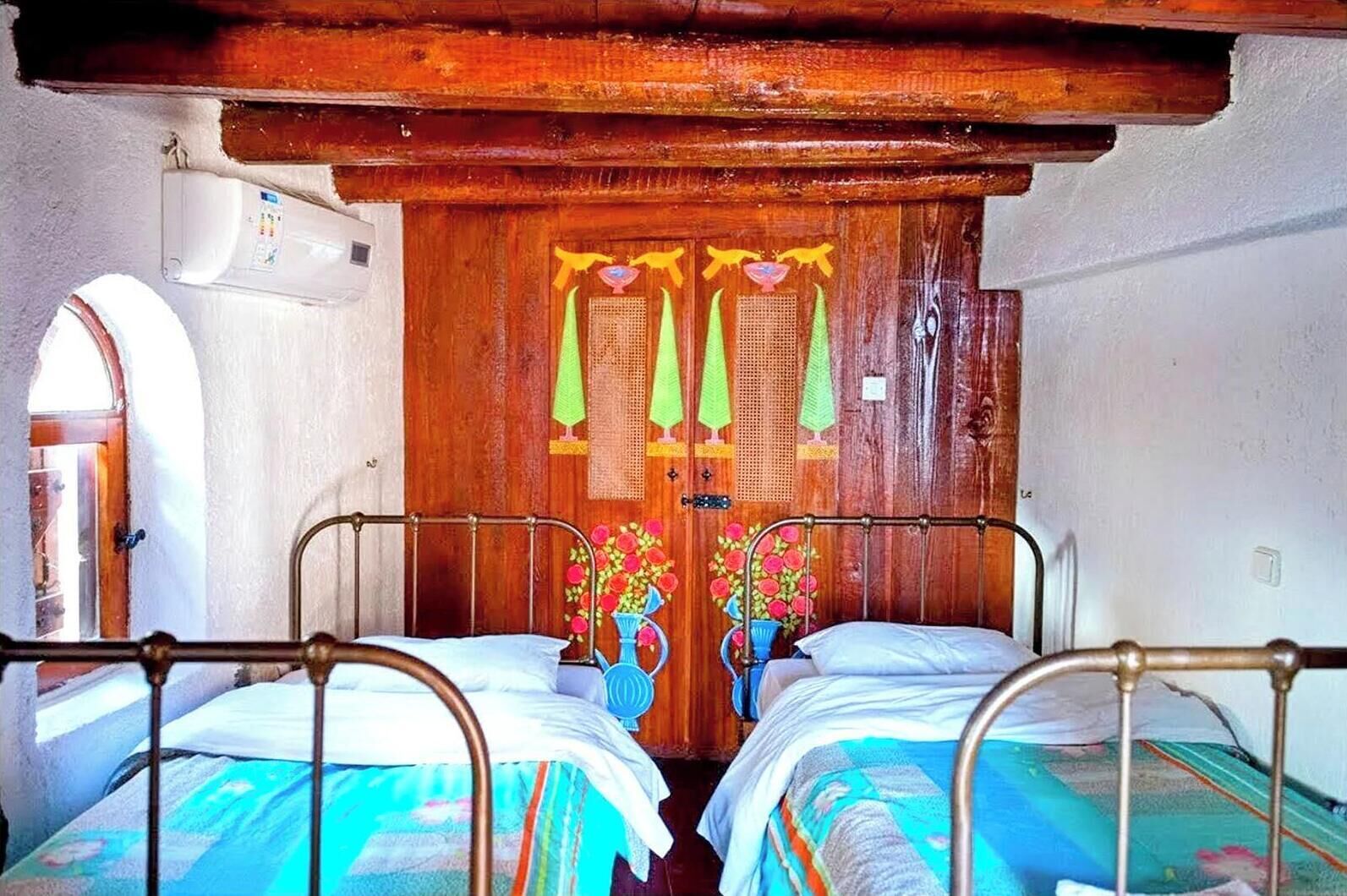 Une pièce avec deux lits en métal, une porte en bois avec un miroir et une petite fenêtre.
