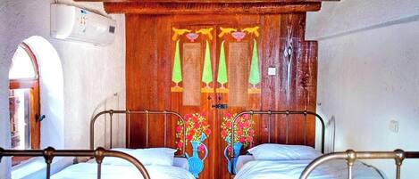 Une pièce avec deux lits en métal, une porte en bois avec un miroir et une petite fenêtre.