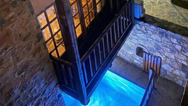 A stone wall, a wooden staircase with a railing, and a pool with blue lighting. - Elounda Monastiri Cretan sea View House With Pool (Agios Nikolaos)