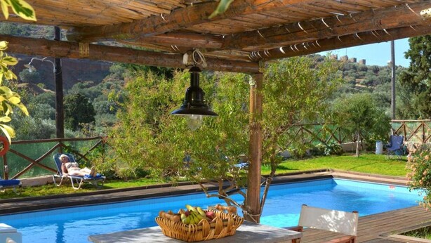 A pool area with a wooden pergola, a lounge chair, and a basket of fruits. - Elounda Collection Villa (Agios Nikolaos)
