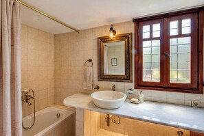 A bathroom with a bathtub, a large sink, a mirror, and a window with frosted glass.