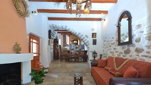 A cozy living room with a fireplace, a stone wall, and a wooden ceiling. - Elounda Collection Villa (Agios Nikolaos)