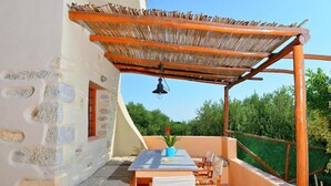 A covered outdoor seating area with a table and chairs, a hanging light fixture, and a view of greenery in the background. - Elounda Collection Villa (Agios Nikolaos)