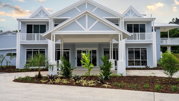 Une maison à deux étages, dotée d’une façade symétrique, d’un porche avant couvert et d’un jardin aménagé avec différentes espèces de plantes.