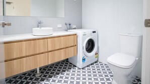 Une salle de bain moderne équipée d’un lavabo, d’un miroir, d’un lave-linge et de toilettes.