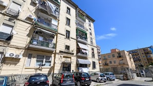 A multi-story residential building with balconies, parked cars, and a clear blue sky. - Domus Romeo - Camera 1 (Naples)